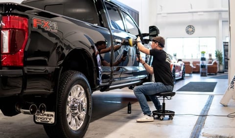 Mechanic detailing a black pickup truck in a service garage, using a buffing tool on the vehicles door
