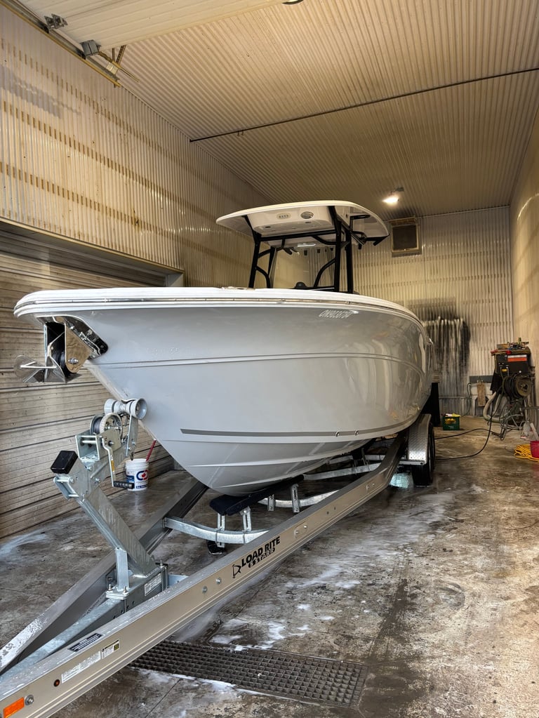 White recreational boat on a metal trailer inside a corrugated metal storage garage with supplies nearby