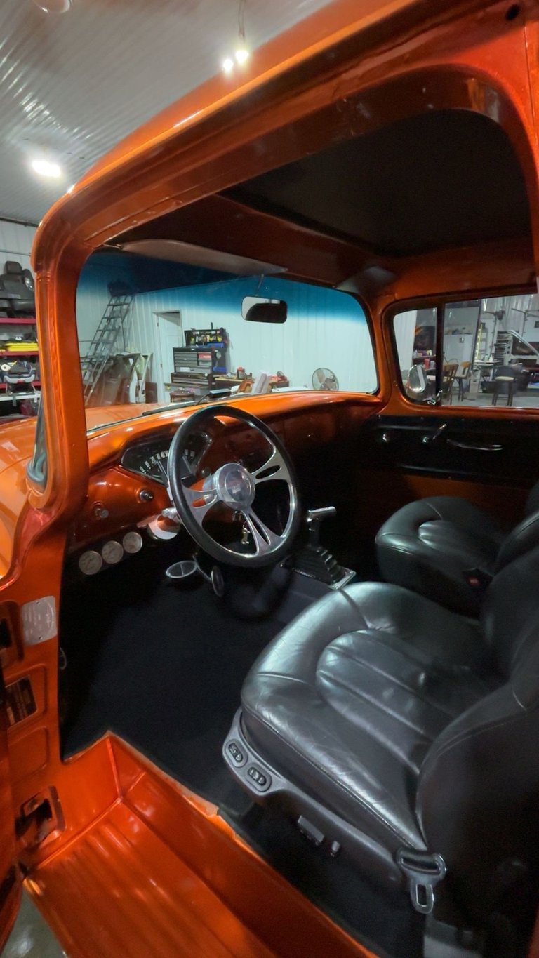 Interior of restored orange hot rod with black leather seats, vintage steering wheel, and dash gauges on display