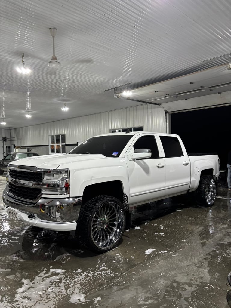 White Chevrolet pickup truck with custom chrome wheels parked in an industrial garage bay
